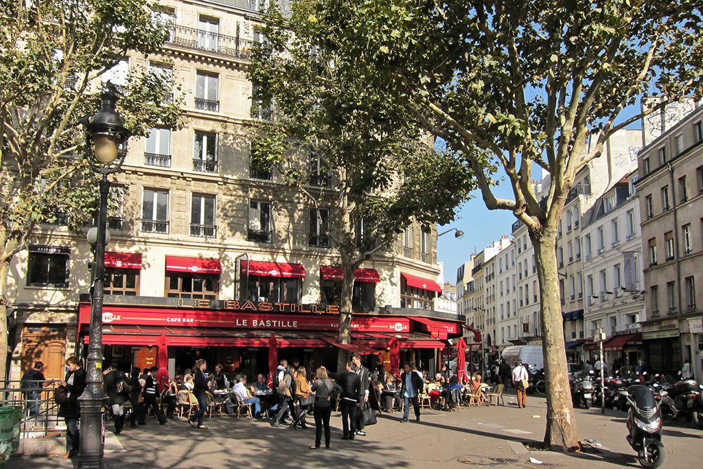 Sunny Paris street scene. Restaurant "La Bastille" visible with red awnings and a neon sign